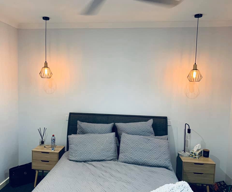 Two geometric wire pendants with warm globes hung either side of a bed as bedside lights