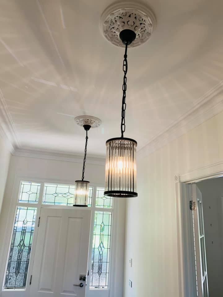 Two glass rod cylinder pendants hanging from ornate ceiling roses in a period entrance hall with a leadlight front door