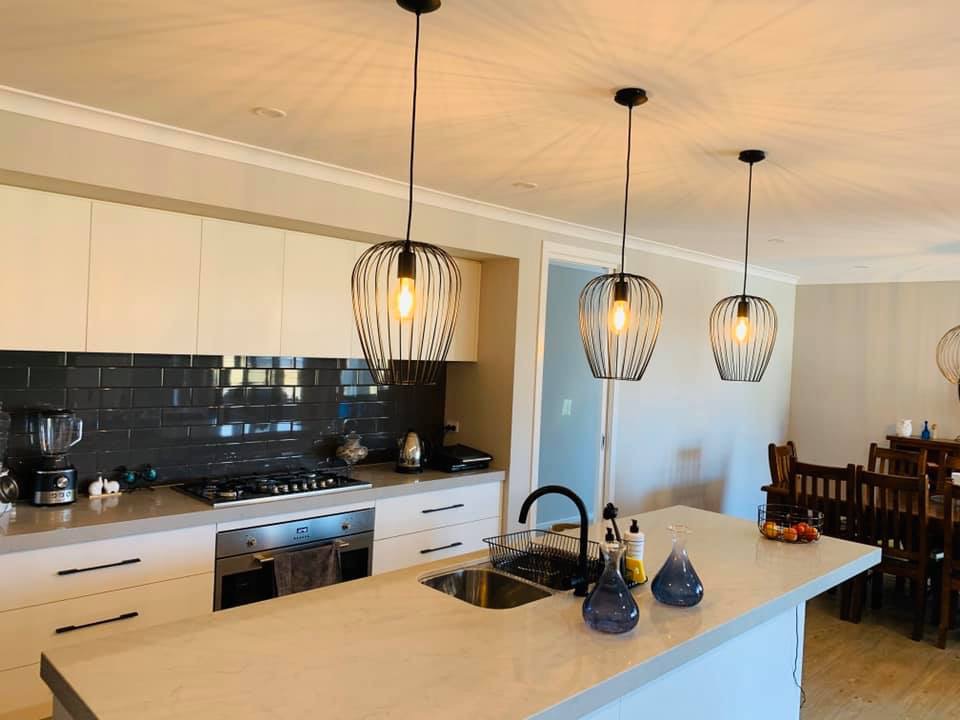 Three black wire cage pendants with filament globes hung over a stone kitchen island